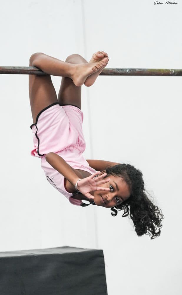 Girl hanging upside down from a bar and waving