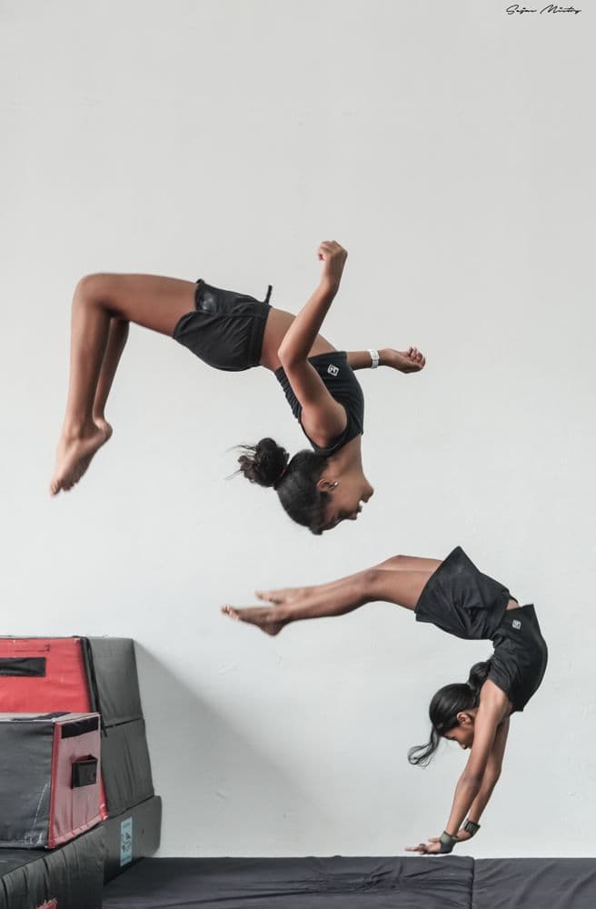 Two girls flipping over soft mats